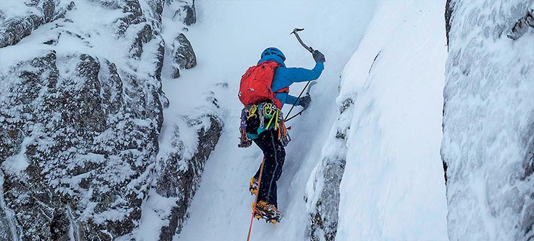 person using ice axe and crampons to climb icy gully